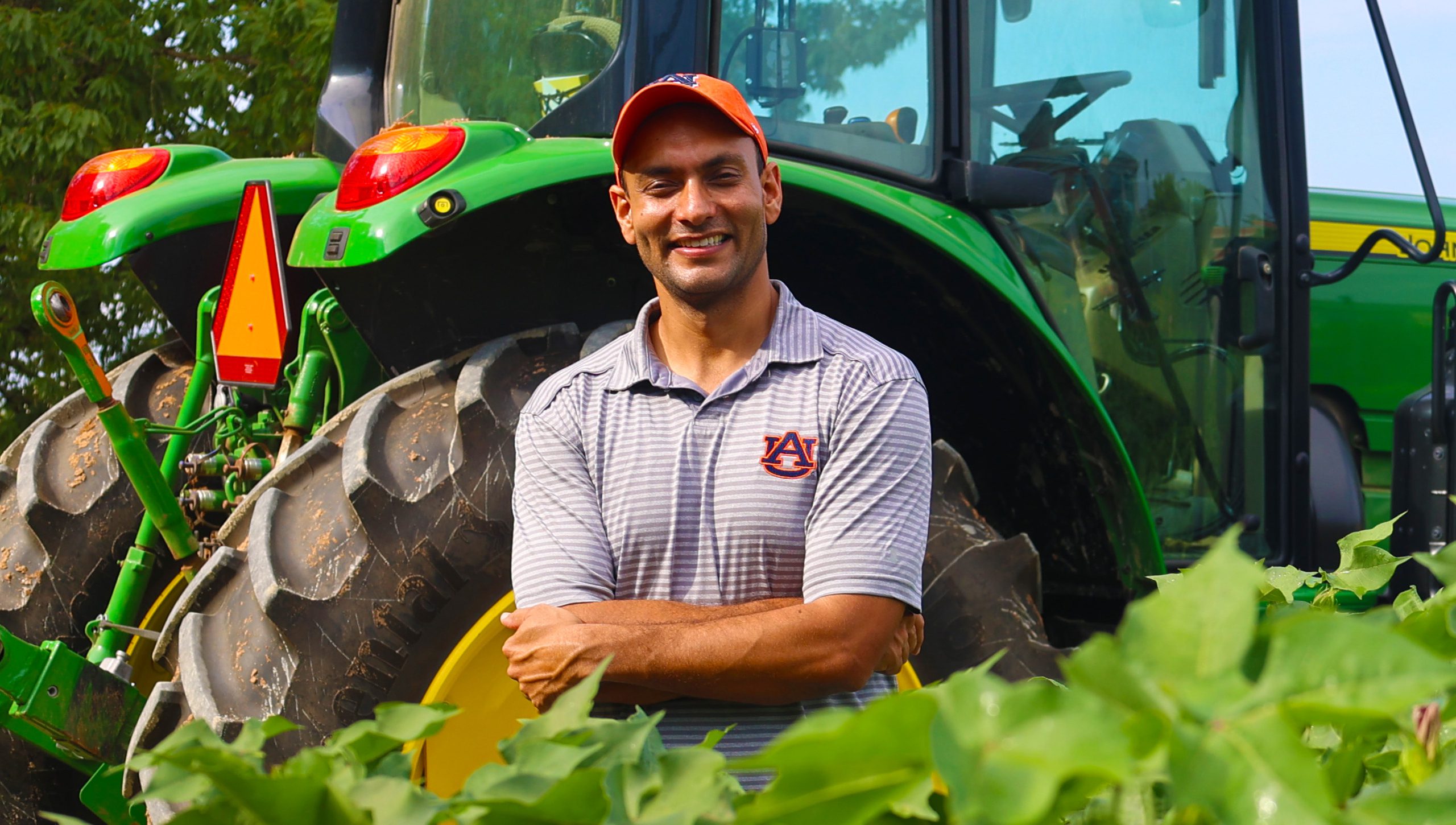 Simerjeet Virk standing in a field next to a green tractor.