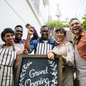 Culturally diverse small business owners proudly standing by "Grand Opening" Sign