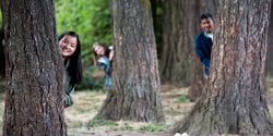 Alabama 4-H kids peaking from behind trees in a forest