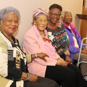 Four older women sit in a row, smiling for the camera