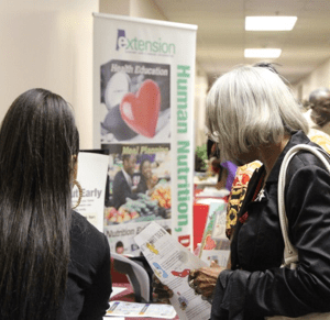 One older African American woman and one younger woman look over an information booth at an SAI conference