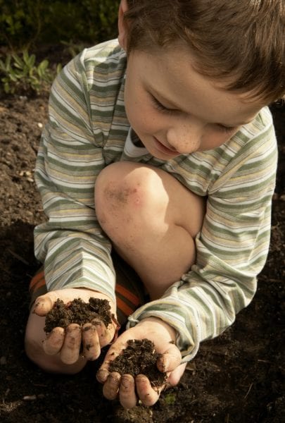 Boy crouching, holding dirt in hands, high angle view