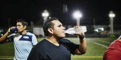 Male soccer player drinking water after nighttime game with friends