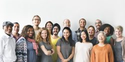 A group of 16 diverse people stand smiling for the camera.