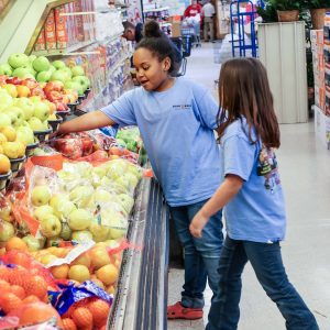 two young girls pick out fruit at grocery store