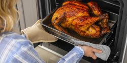 A woman taking a roasted turkey out of an oven.