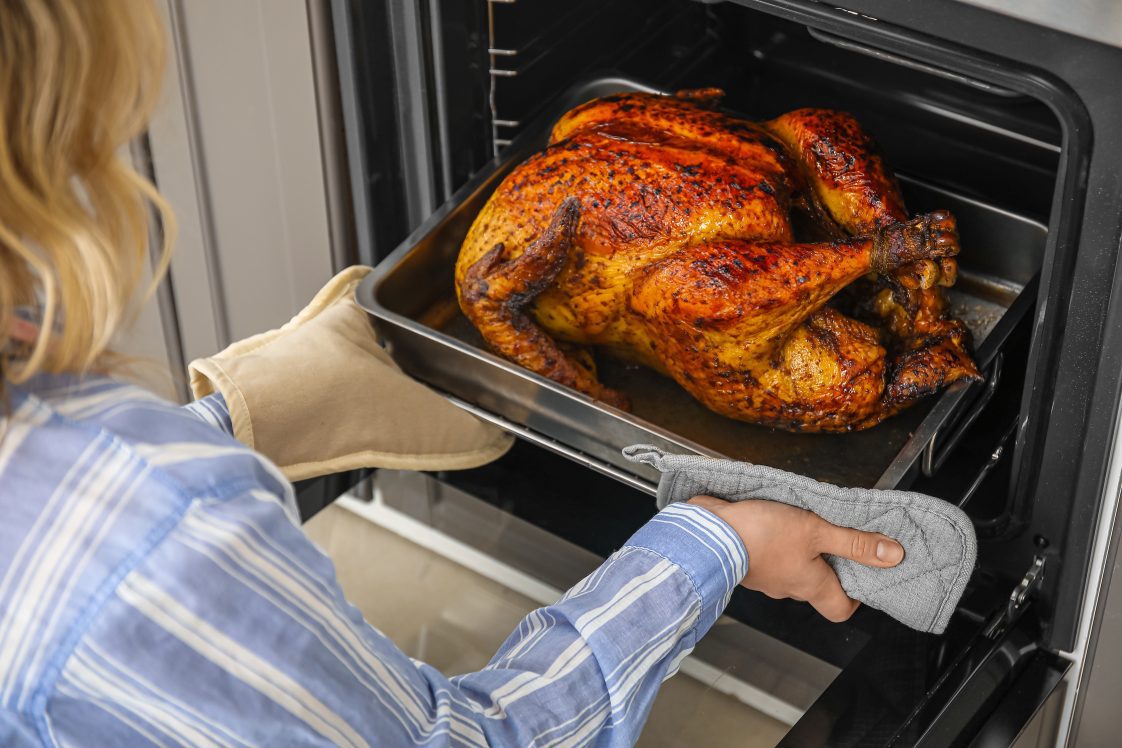 A woman taking a roasted turkey out of an oven.