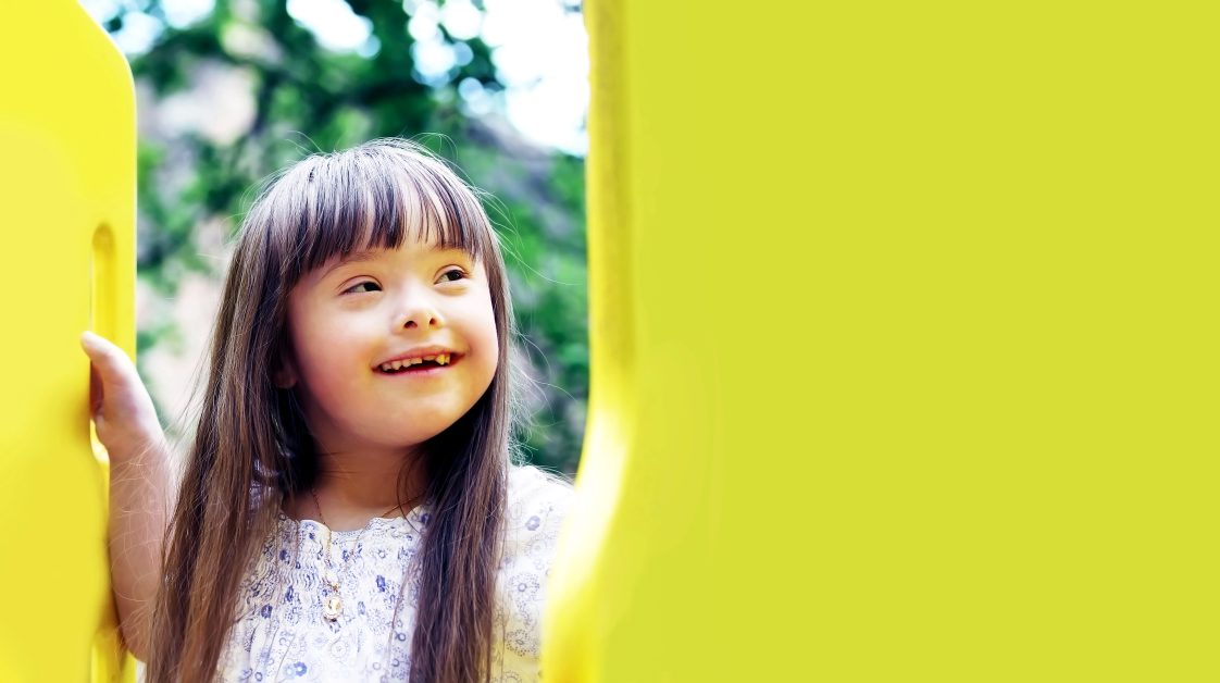 A young girl sitting on a yellow slide on a playground.