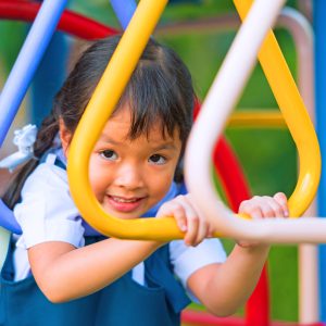 A young girl with pigtails playing on monkey bars on a playground.