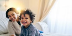 A young Black mother and her toddler playing on the bed.