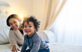 A young Black mother and her toddler playing on the bed.