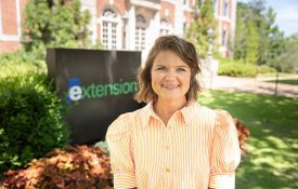 Maggie Thompson standing in front of the Extension sign at Duncan Hall on Auburn University's campus