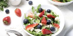 salad with strawberries, blueberries, arugula and feta cheese on white plate.