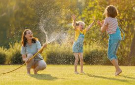 A mother and two daughters playing in the yard, with the mother spraying the girls with a water hose.