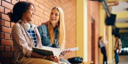 Two high school girls laughing and talking while sitting on a bench.