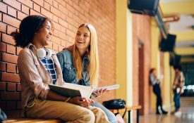 Two high school girls laughing and talking while sitting on a bench.