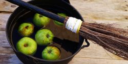 A black cauldron filled with water and green apples with a broom lying across the top of it.