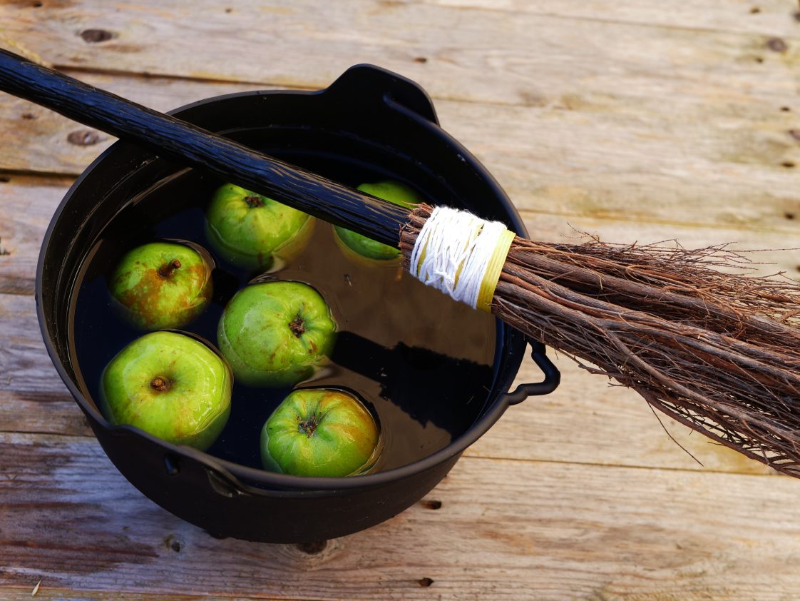 A black cauldron filled with water and green apples with a broom lying across the top of it.