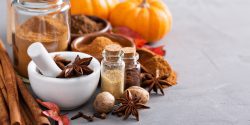 An assortment of fall spices along with leaves and pumpkins on a gray table top.