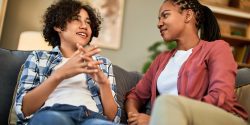 A teenage boy talking to his mother while sitting on a couch.