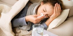 A sick woman lying on a couch and using a tissue.