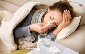 A sick woman lying on a couch and using a tissue.