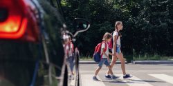 Two kids walking in a crosswalk in front of a car.