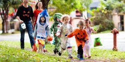 A group of children and two adults walking on a sidewalk wearing Halloween costumes.