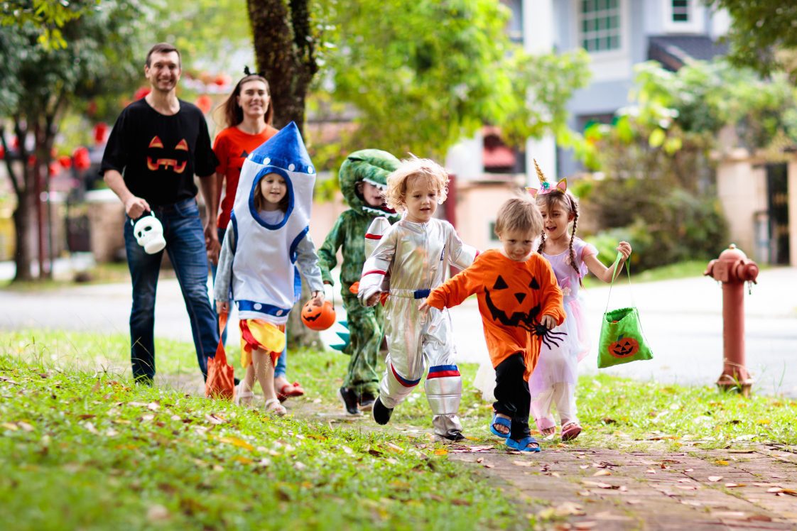 A group of children and two adults walking on a sidewalk wearing Halloween costumes.