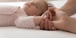 baby sleeping on their back and holding an adult hand