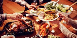 A Thanksgiving table scene, where someone is carving a turkey and putting the meat on someone's plate.