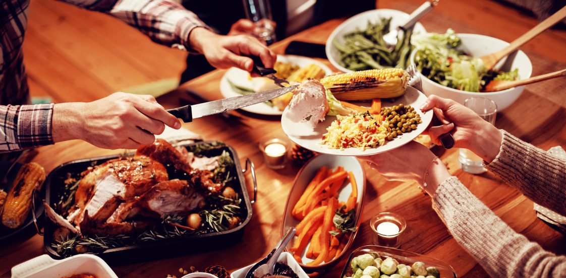 A Thanksgiving table scene, where someone is carving a turkey and putting the meat on someone's plate.