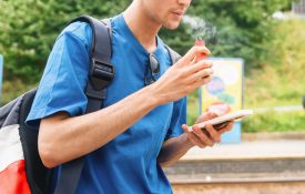 young man wearing a backpack and looking at his phone while using a vape device