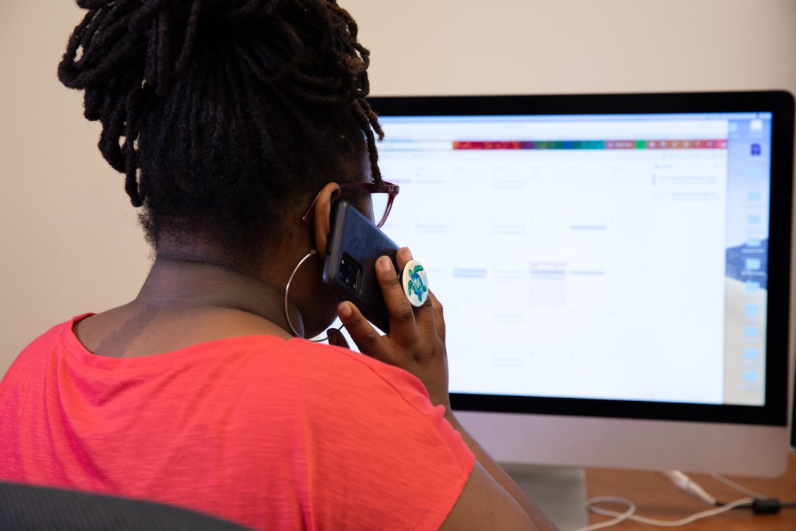 A younger woman talking on the phone while on the computer.