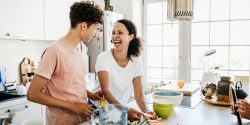 A mom at home in the kitchen, laughing while preparing some lunch with her son.