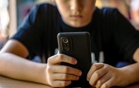 A teenage boy holding a cell phone while sitting at a table.