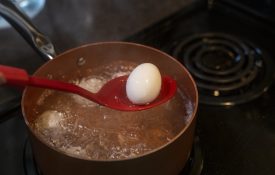 A red spoon getting an egg out of boiling water.