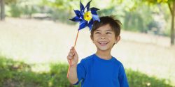 A smiling, young boy holding a blue pinwheel for Child Abuse Prevention Month.
